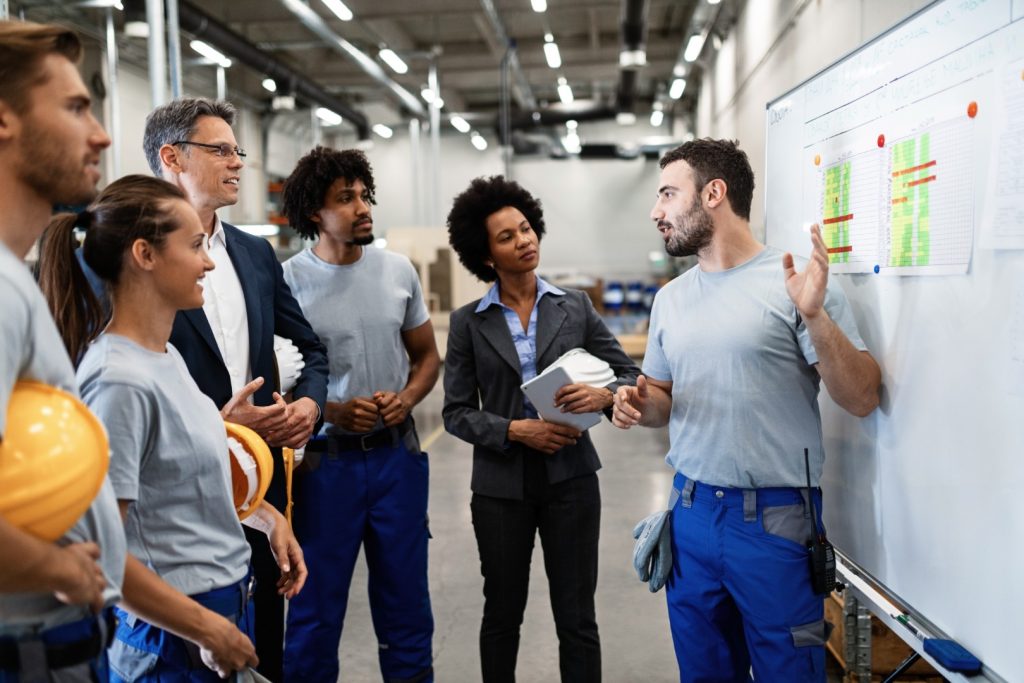 jovem trabalhador manual apresentando nova estrategia de negocios para gerentes de empresa e seus colegas em uma fabrica Grande